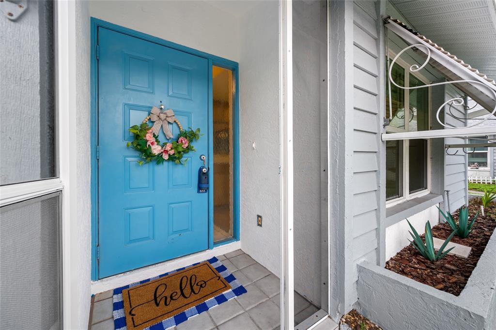 A bright blue front door with a floral wreath sits beside a small garden bed — 2060 SHEFFIELD COURT, OLDSMAR, FL