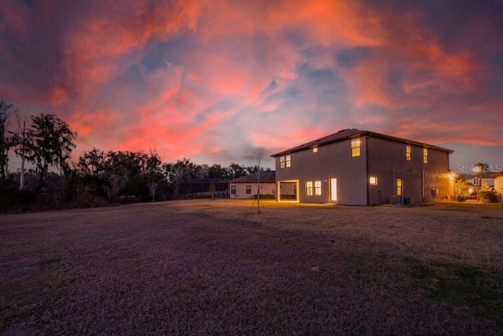 A two-story house exterior viewed from a large, grassy backyard at sunset — 14604 HORSE TROT ROAD, LITHIA, FL
