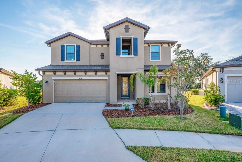 A two-story suburban house with a beige stucco exterior, blue shutters, and a concrete driveway — 14604 HORSE TROT ROAD, LITHIA, FL