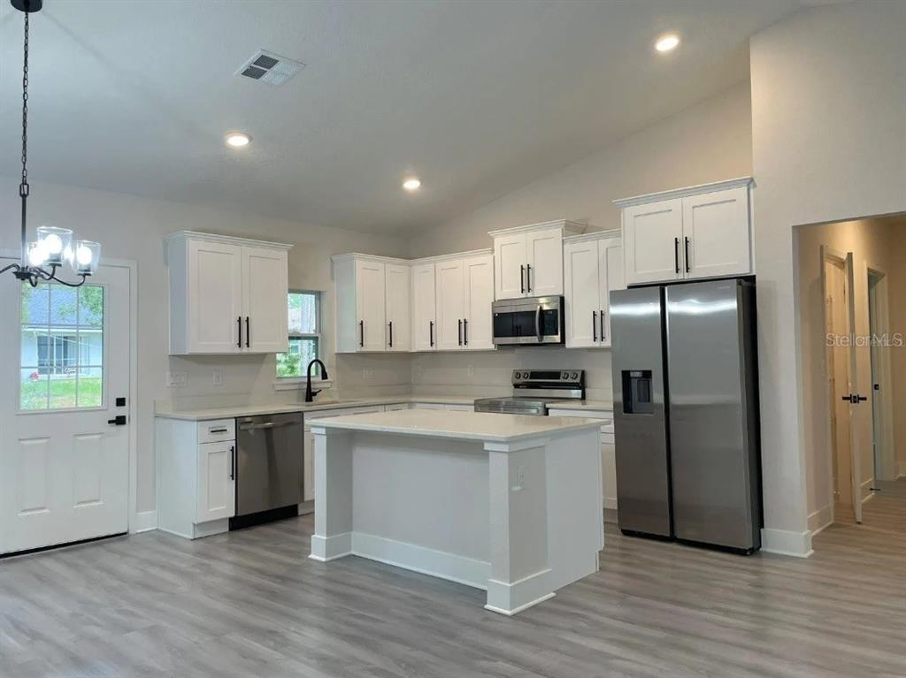 A modern kitchen features white cabinetry, stainless steel appliances, a center island, and gray flooring — 6817 SW 131ST PLACE, OCALA, FL