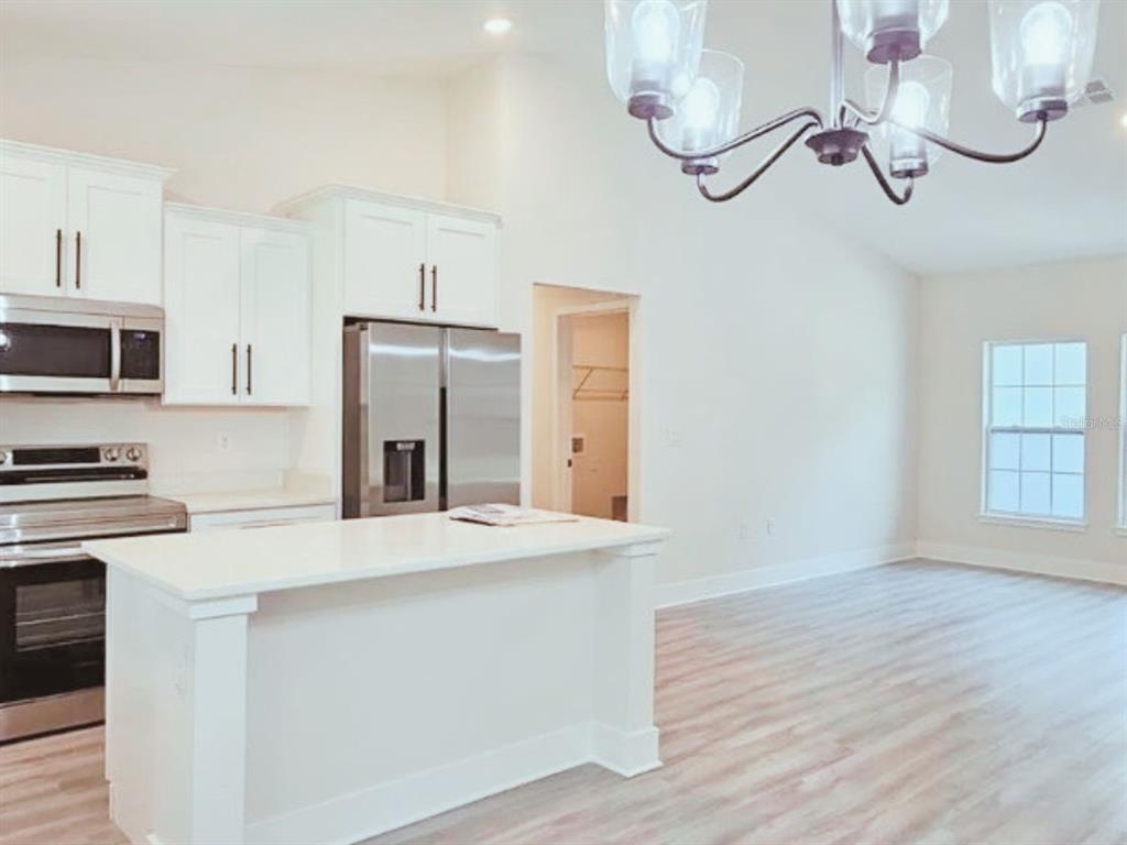 A kitchen with white cabinets, stainless steel appliances, and an island opens to a living area — 6817 SW 131ST PLACE, OCALA, FL