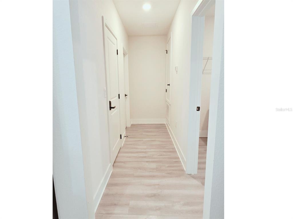 A hallway with light wood-look flooring, white walls, and several closed interior doors — 6817 SW 131ST PLACE, OCALA, FL