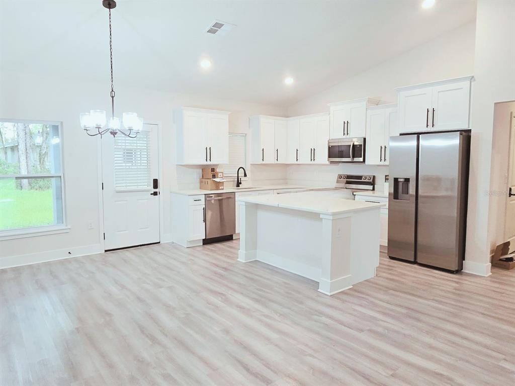 A bright kitchen features white cabinets, stainless steel appliances, a center island, and light flooring — 6817 SW 131ST PLACE, OCALA, FL