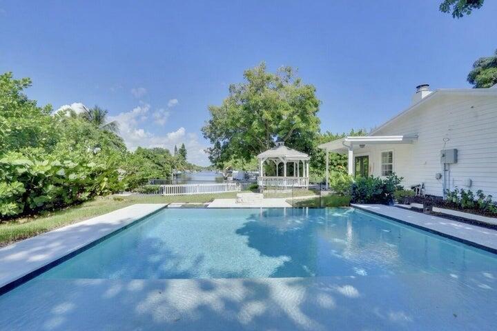 A swimming pool sits in the backyard of a white house with a gazebo nearby — 1808 N 17th Ave Avenue N, FL 33460, FL