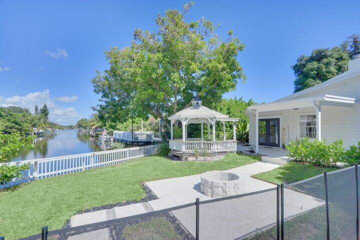 A backyard with a white gazebo, a stone fire pit, and a view of a canal — 1808 N 17th Ave Avenue N, FL 33460, FL