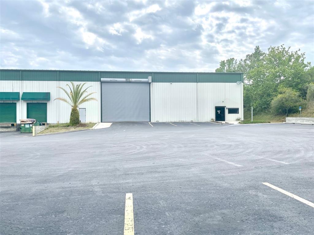 A commercial warehouse building features a large roll-up door, a pedestrian entrance, and asphalt parking — 19994 INDEPENDENCE BOULEVARD, GROVELAND, FL