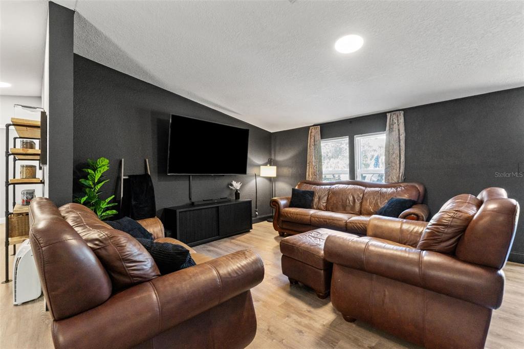 A living room features dark gray walls, brown leather furniture, and light wood-look flooring — 6886 W EDGEWOOD LANE, HOMOSASSA, FL