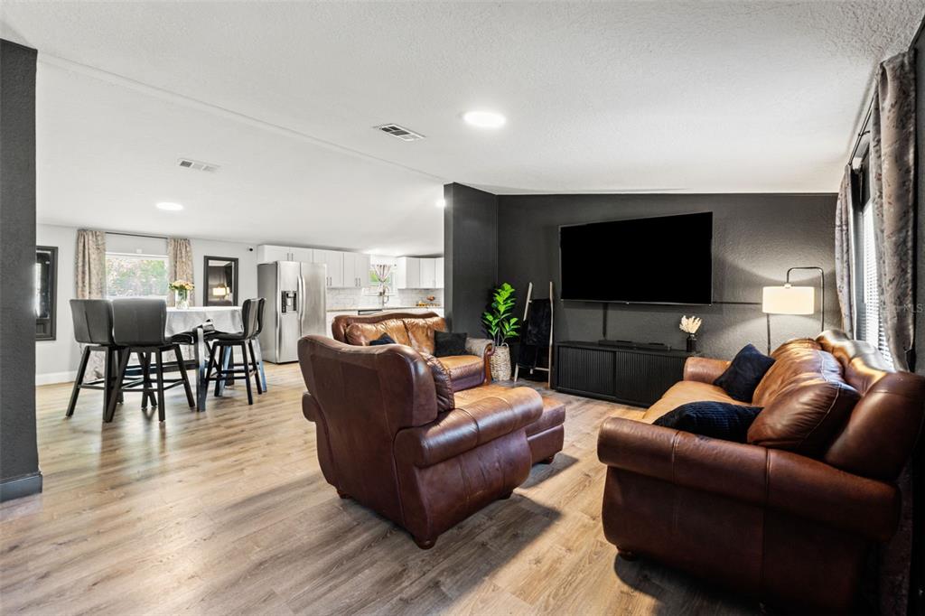 A living room with leather furniture and a television opens to a dining area — 6886 W EDGEWOOD LANE, HOMOSASSA, FL