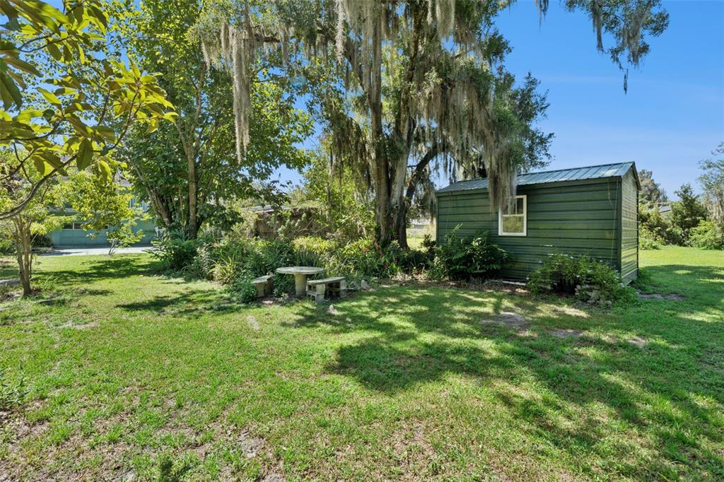 A green metal shed sits in a grassy backyard near a stone table and trees — 1730 NEPTUNE ROAD, KISSIMMEE, FL