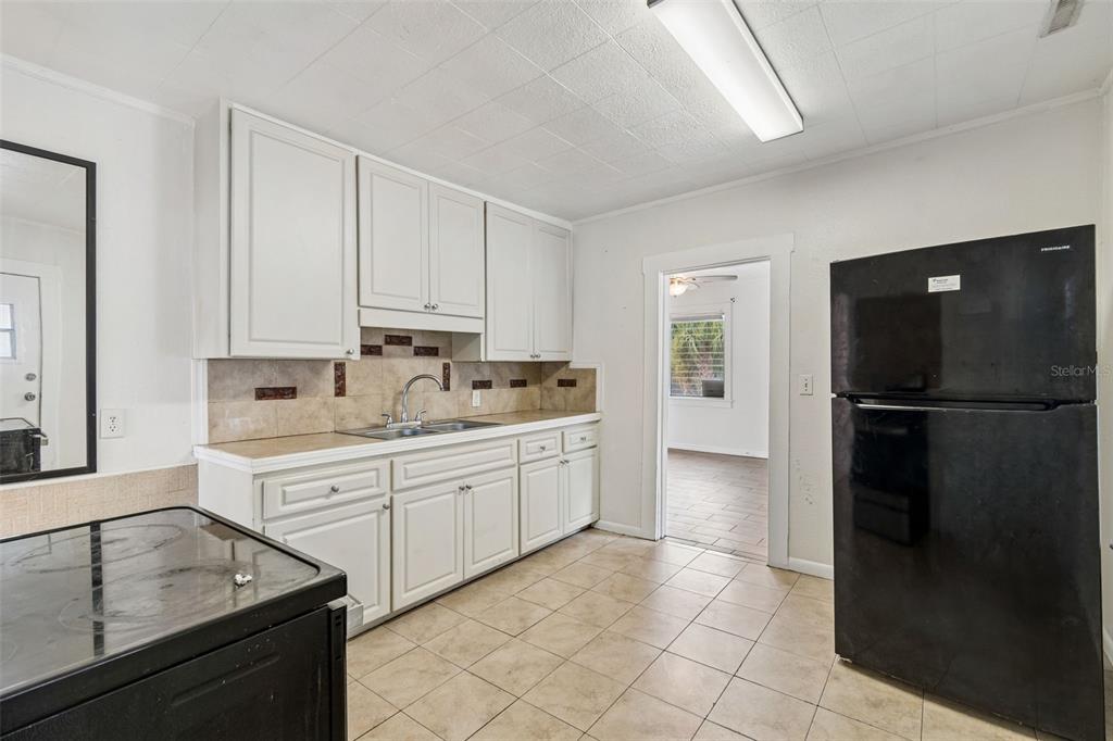 A kitchen features white cabinets, tan tile flooring, a black refrigerator, and a black stove — 1363 TIOGA AVENUE, CLEARWATER, FL