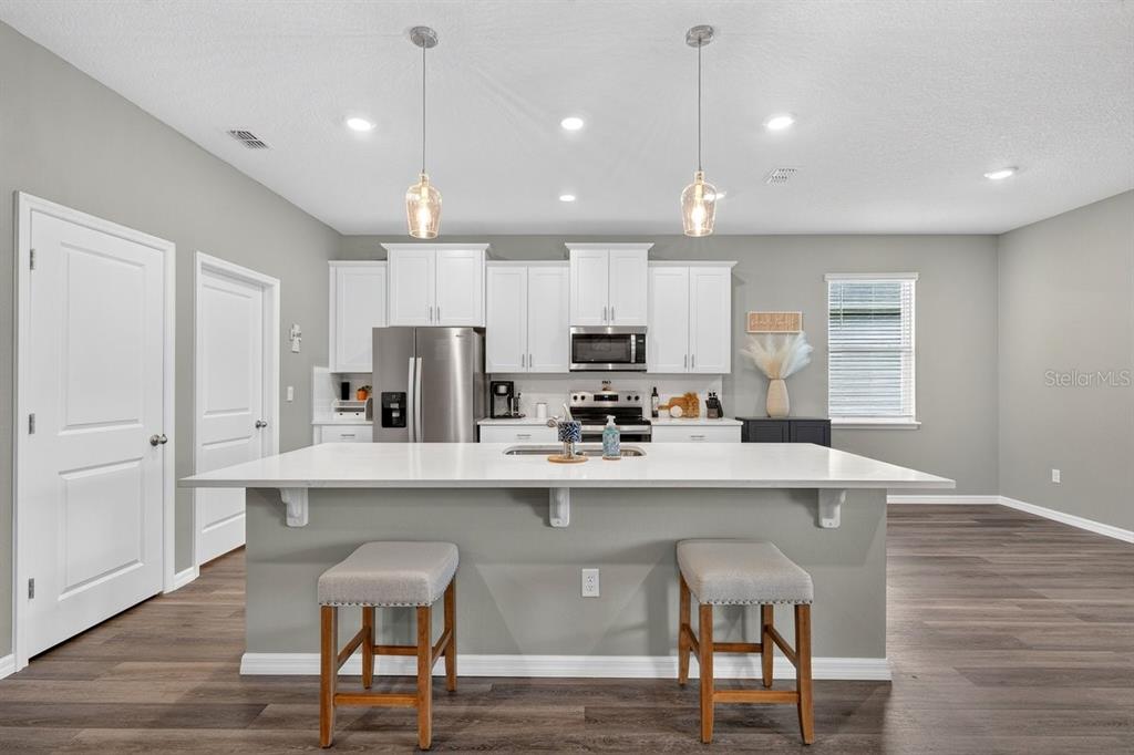 A modern kitchen features white cabinets, a large island with two stools, and stainless appliances — 349 ROVER ROAD, ORMOND BEACH, FL