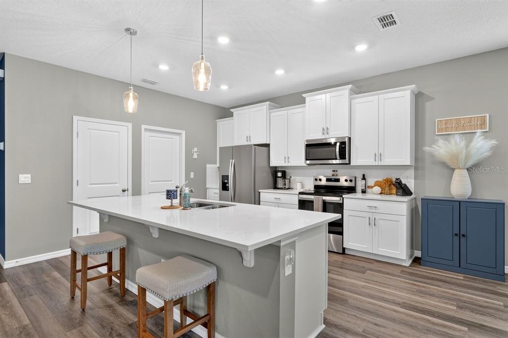 A kitchen features white cabinets, stainless steel appliances, a quartz-topped island, and wood-look flooring — 349 ROVER ROAD, ORMOND BEACH, FL