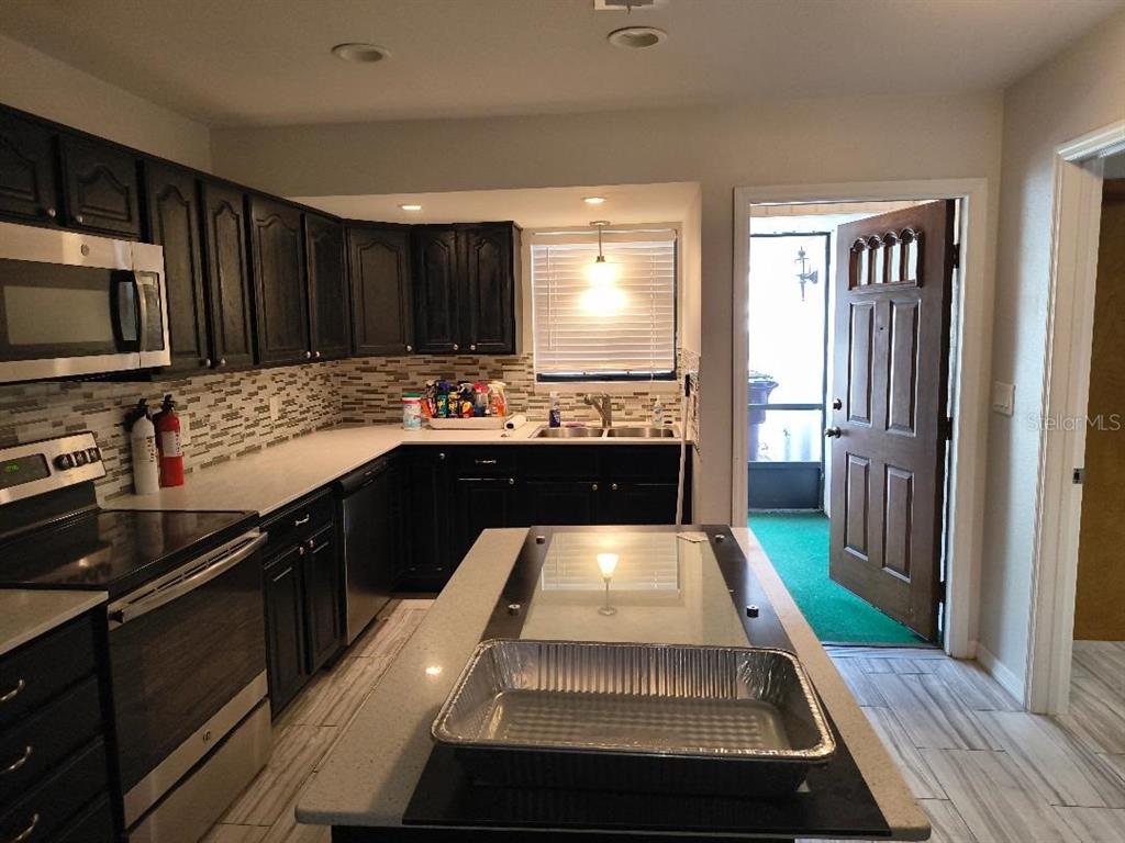 A kitchen features dark cabinets, light countertops, a central island, and a door to a porch — 1120 N ILLINOIS AVENUE, ST CLOUD, FL