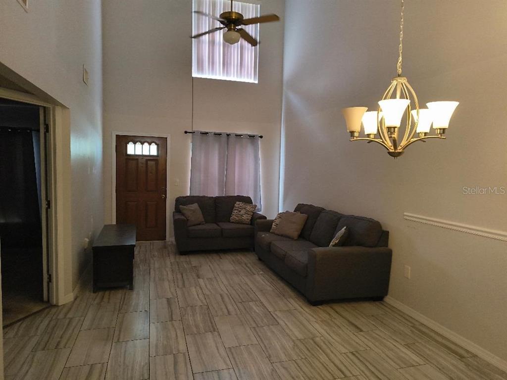 A living room features high ceilings, tile flooring, a chandelier, and two gray sofas — 1120 N ILLINOIS AVENUE, ST CLOUD, FL