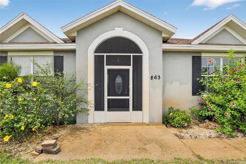 The exterior of a house features a screened front entryway and two flowering bushes — 863 C F KINNEY ROAD, LAKE WALES, FL