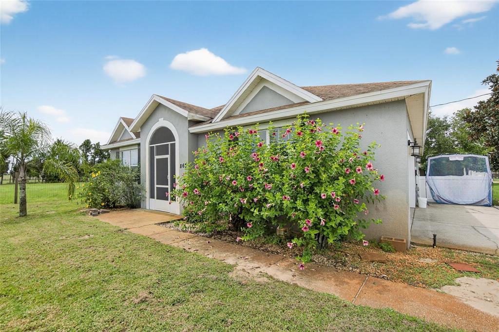 A single-story house with a grey stucco exterior, a screened entryway, and a flowering bush — 863 C F KINNEY ROAD, LAKE WALES, FL