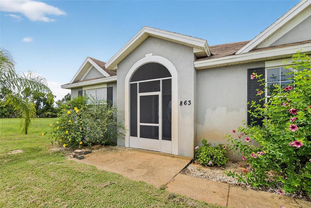 The exterior of a house features a screened entryway, stucco walls, and a landscaped yard — 863 C F KINNEY ROAD, LAKE WALES, FL