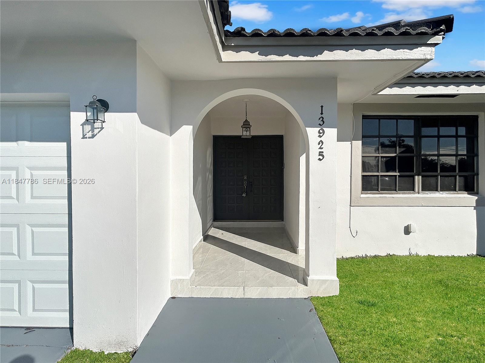 The exterior of a white house features a covered arched entryway and a dark door — 13925 SW 26th Ter, Miami FL 33175, MIAMI, FL