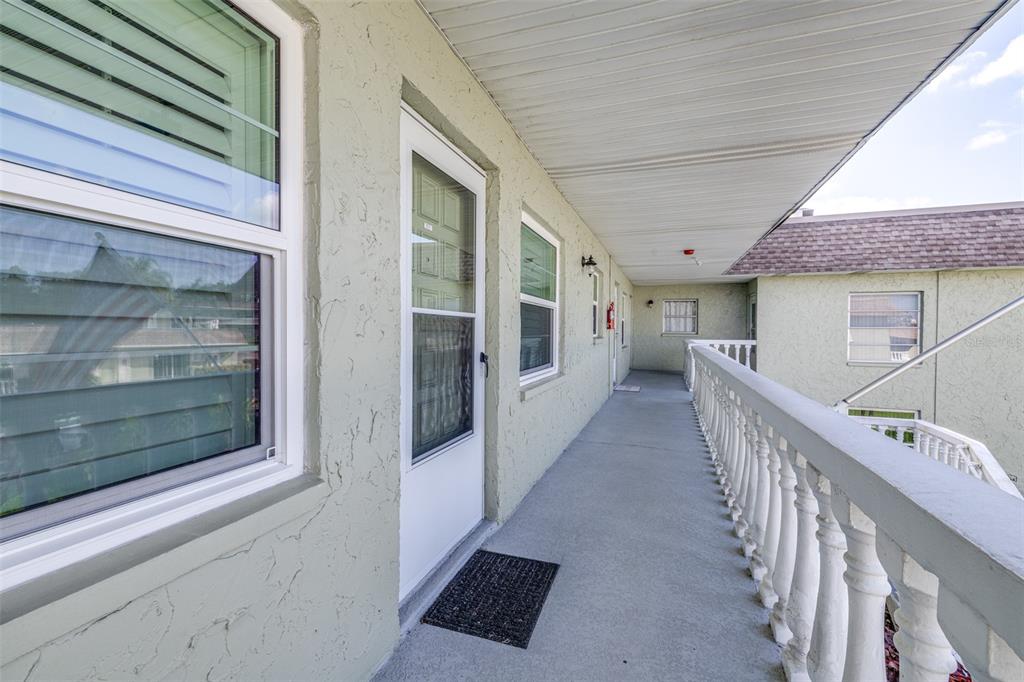 An outdoor balcony walkway with a white railing, stucco walls, and several unit doors — 1250 S PINELLAS AVENUE UNIT 711, TARPON SPRINGS, FL