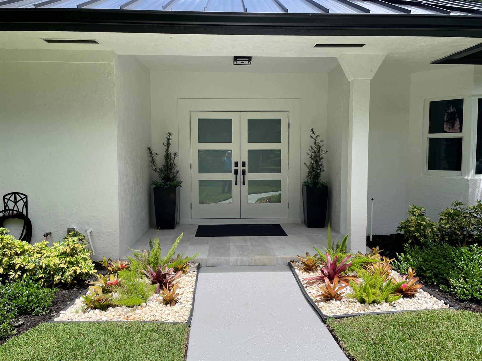 A modern white home entrance features double glass doors, potted plants, and a stone walkway — 18457 SE Heritage Oaks Lane, Jupiter FL 33469, JUPITER, FL
