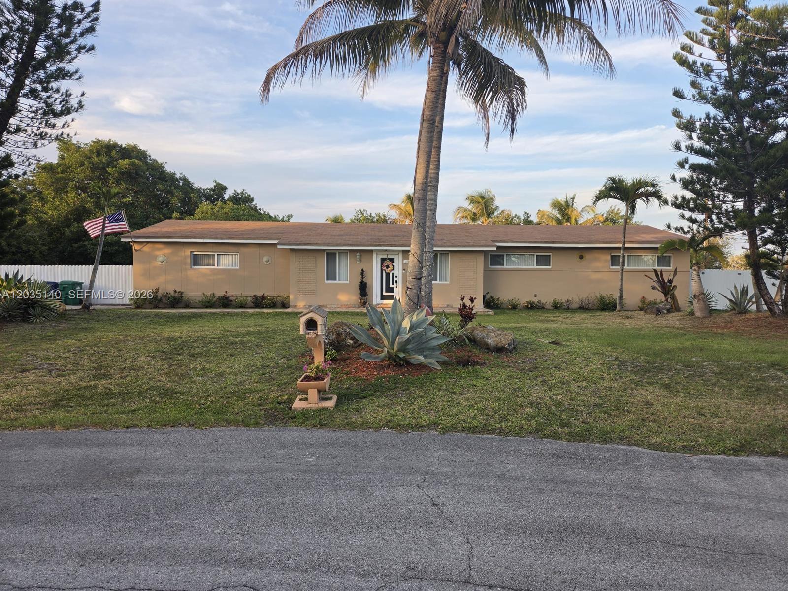 A single-story tan house with a palm tree in the front yard and an American flag — 17405 SW 109th Ct, Miami FL 33157, MIAMI, FL