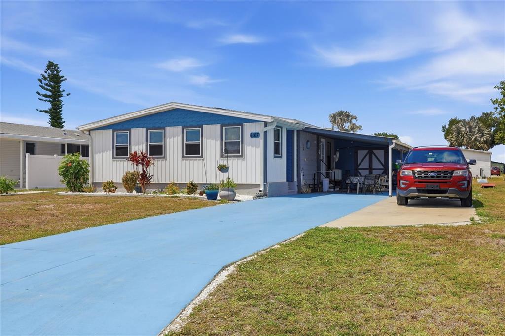 A single-story manufactured home with a blue-painted driveway and a red SUV parked underneath — 6167 ORIOLE BOULEVARD, ENGLEWOOD, FL