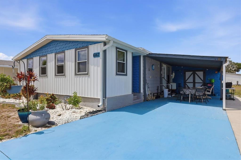 A single-story manufactured home features white vertical siding, blue accents, and a covered carport — 6167 ORIOLE BOULEVARD, ENGLEWOOD, FL
