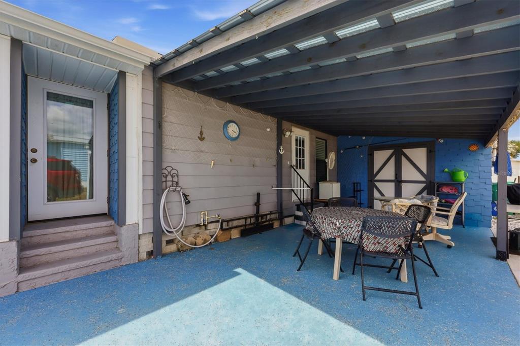 A covered outdoor patio with blue flooring, a dining set, and a gray wall — 6167 ORIOLE BOULEVARD, ENGLEWOOD, FL