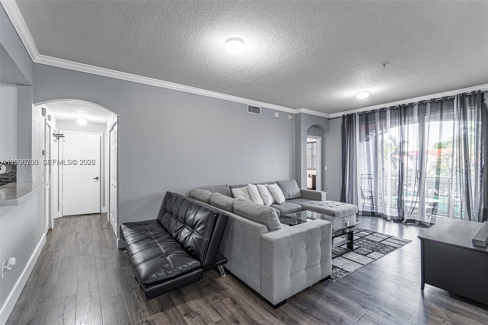 A living room features gray walls, wood-look flooring, a sectional sofa, and a black futon — 6340 NW 114th Ave # 134, Doral FL 33178, DORAL, FL