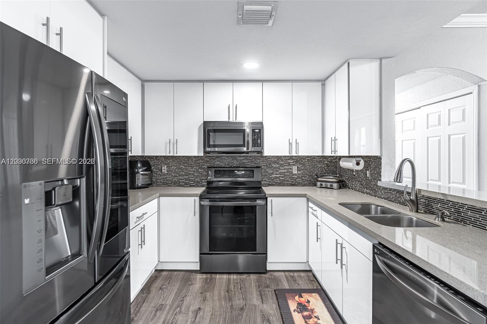 A modern kitchen features white cabinets, stainless steel appliances, and a dark tiled backsplash — 6340 NW 114th Ave # 134, Doral FL 33178, DORAL, FL