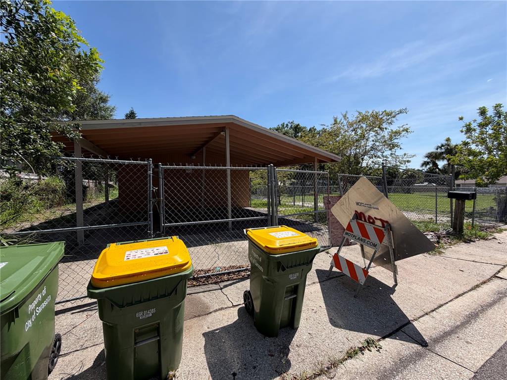 A chain-link fence encloses a carport and a vacant lot with two trash bins — 1764 24TH STREET, SARASOTA, FL