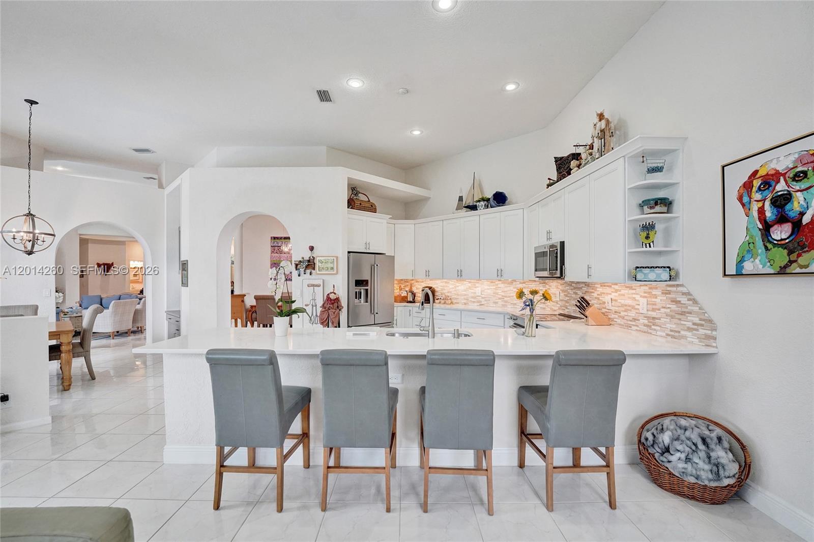A kitchen features white cabinets, a quartz island with four gray stools, and tile flooring — 1640 Island Way, Weston FL 33326, WESTON, FL