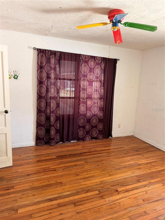 An empty room features hardwood floors, purple patterned curtains, and a colorful multi-blade ceiling fan — 1129 HOLLY AVENUE, DAYTONA BEACH, FL