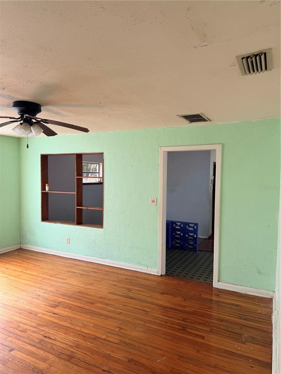 A room with light green walls, hardwood floors, a ceiling fan, and an open wall cutout — 1129 HOLLY AVENUE, DAYTONA BEACH, FL