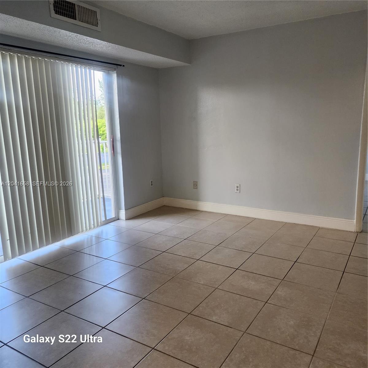 An empty room features light-colored tile flooring, gray walls, and a sliding glass door — 8200 SW 210th St # 111, Cutler Bay FL 33189, CUTLER BAY, FL