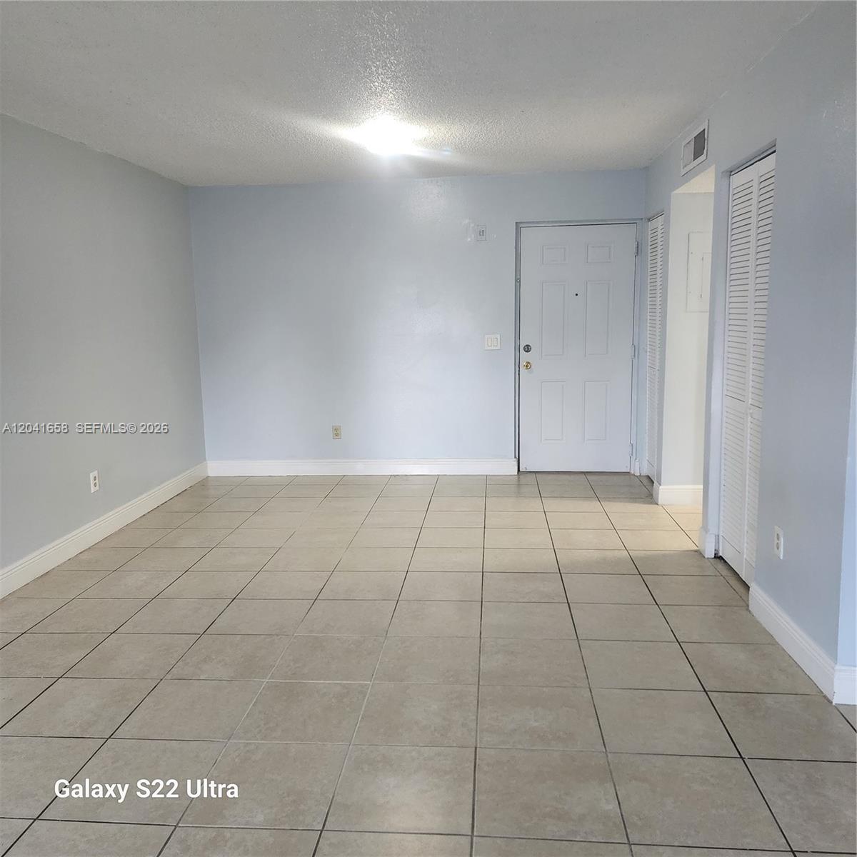 An empty room features light blue walls, beige tile flooring, and a white entry door — 8200 SW 210th St # 111, Cutler Bay FL 33189, CUTLER BAY, FL