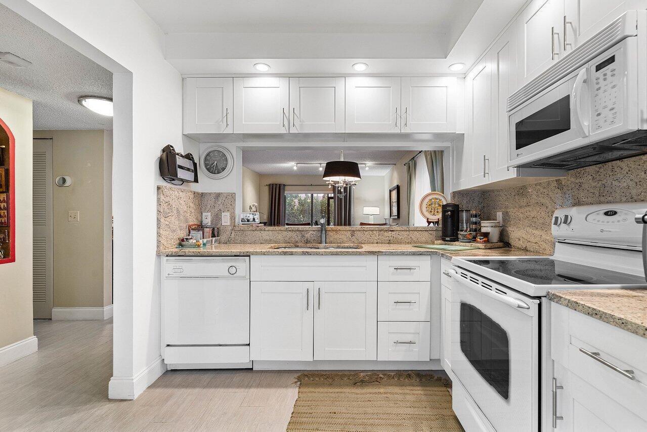 A kitchen features white cabinets, granite countertops, a white dishwasher, and a white oven — 5200 E Club Circle # 106, Boca Raton FL 33487, BOCA RATON, FL