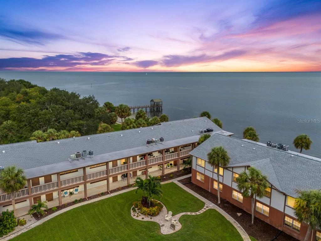 An aerial view of a multi-story apartment building situated along a waterfront at sunset — 650 PINELLAS POINT DRIVE S UNIT 122, ST PETERSBURG, FL