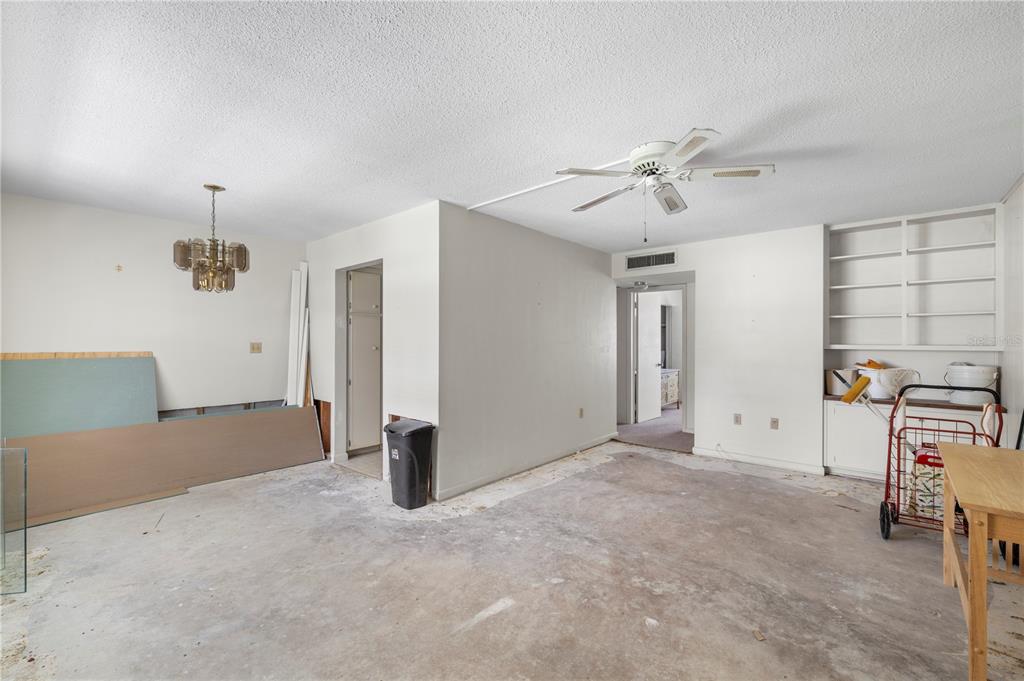 An unfinished room with a ceiling fan, a chandelier, built-in shelving, and exposed concrete flooring — 650 PINELLAS POINT DRIVE S UNIT 122, ST PETERSBURG, FL