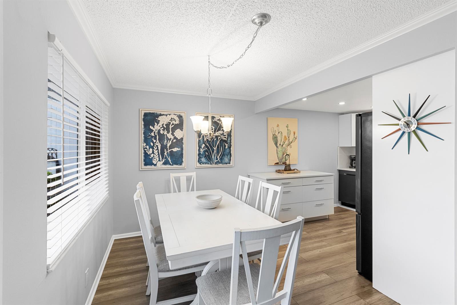 A dining room features a white table, six chairs, a chandelier, and a mid-century clock — 1032 Ventnor H Crescent # H, Deerfield Beach FL 33442, DEERFIELD BEACH, FL