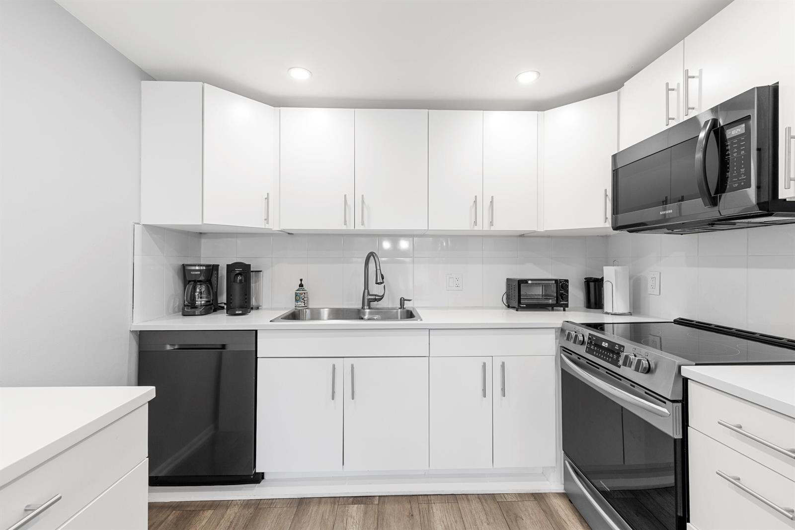 A kitchen features white cabinetry, a stainless steel sink, and black appliances against white walls — 1032 Ventnor H Crescent # H, Deerfield Beach FL 33442, DEERFIELD BEACH, FL