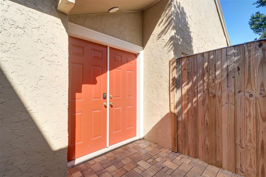 A pair of orange double doors opens onto a small brick-paved patio beside a fence — 4451 TIDAL POND ROAD, NEW PORT RICHEY, FL