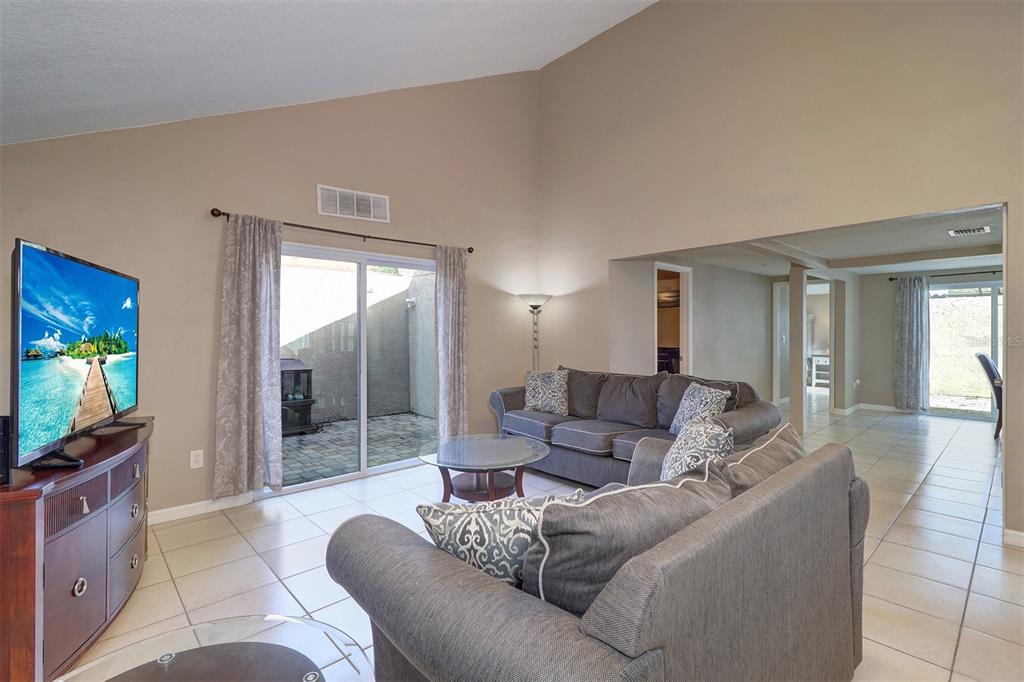 A living room with vaulted ceilings, tile flooring, a sliding glass door, and gray furniture — 4451 TIDAL POND ROAD, NEW PORT RICHEY, FL