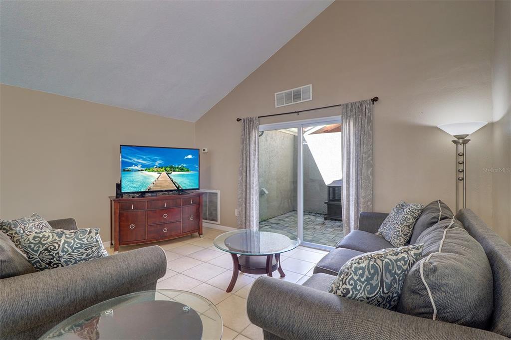 A living room with vaulted ceilings, tile floors, a television console, and a sliding glass door — 4451 TIDAL POND ROAD, NEW PORT RICHEY, FL