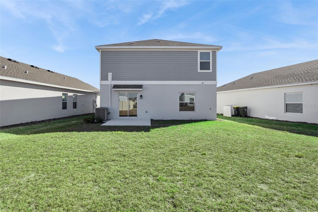 The back exterior of a two-story house features gray siding, a small patio, and grass — 2916 TRANSFORMATION WAY, CLERMONT, FL