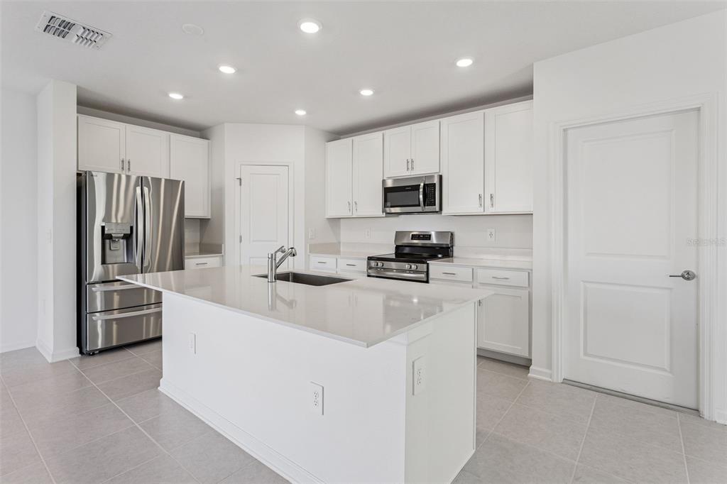 A modern kitchen features white cabinets, stainless steel appliances, a center island, and tile flooring — 2916 TRANSFORMATION WAY, CLERMONT, FL
