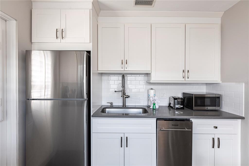 A small kitchen features white cabinets, stainless steel appliances, a gray countertop, and subway tile — 6020 MIDNIGHT PASS ROAD UNIT 31, SARASOTA, FL