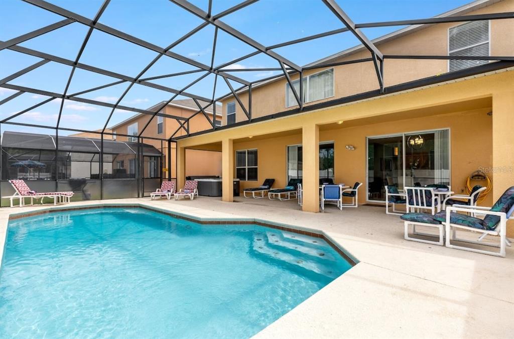 A swimming pool with a screened-in lanai and patio furniture sits behind a two-story house — 1315 SEASONS BOULEVARD, KISSIMMEE, FL