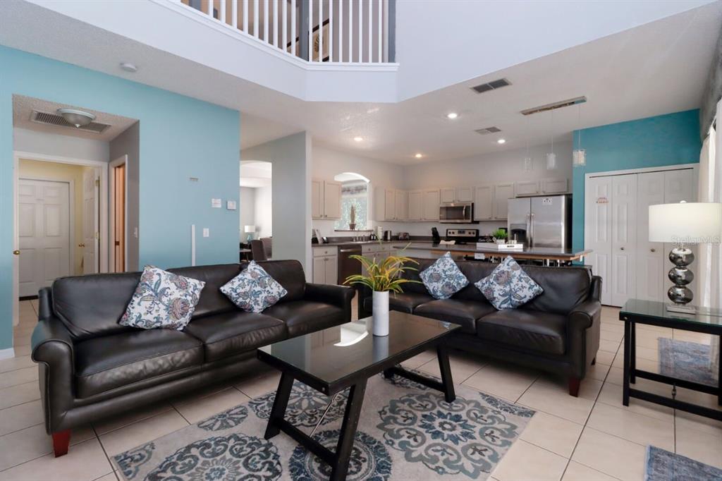 A living room with two dark leather sofas, a glass coffee table, and an open kitchen — 1315 SEASONS BOULEVARD, KISSIMMEE, FL