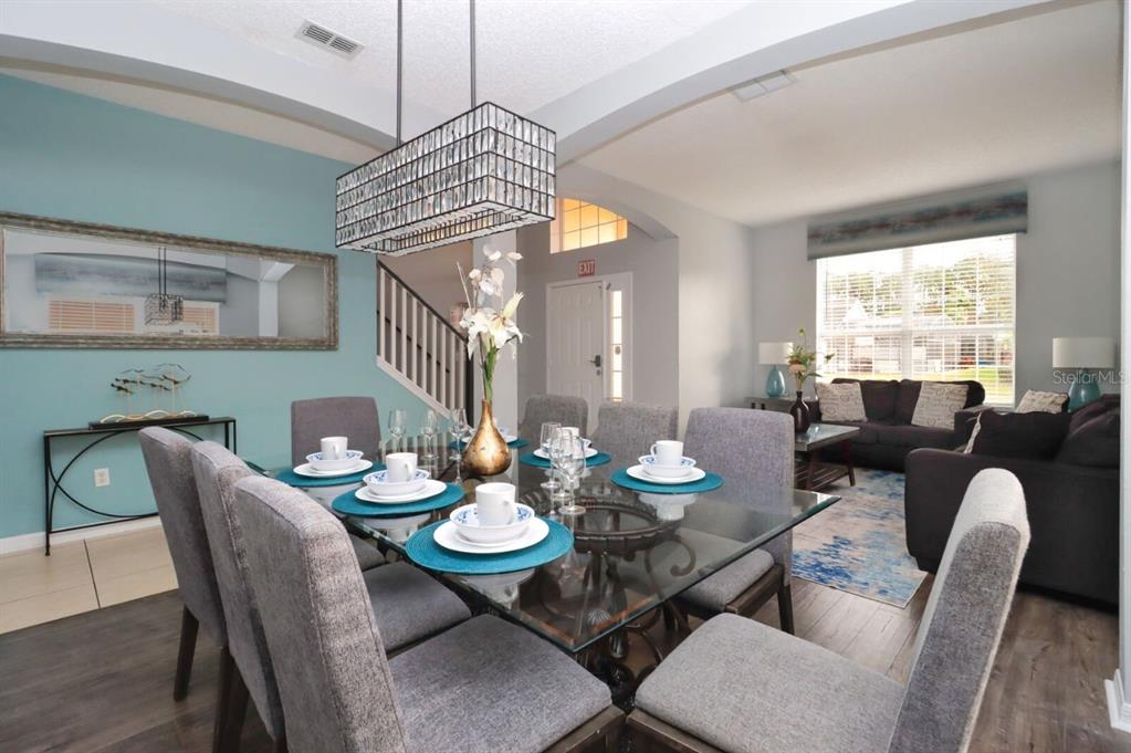 A dining room with a glass table and gray chairs sits adjacent to a living area — 1315 SEASONS BOULEVARD, KISSIMMEE, FL